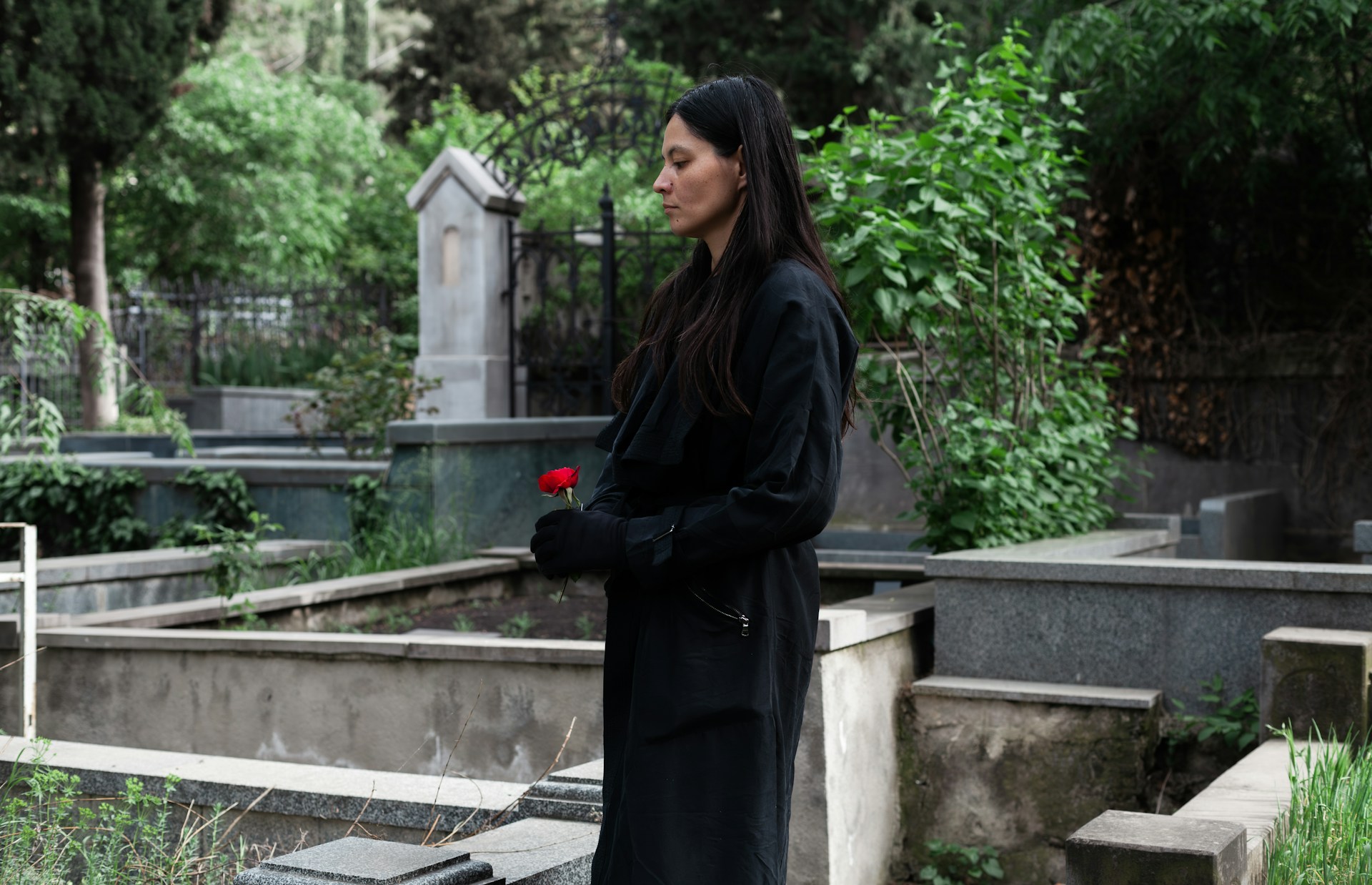 A woman dressed in black holding a red rose and looking down at a gravesite, representing will validity and challenges in BC