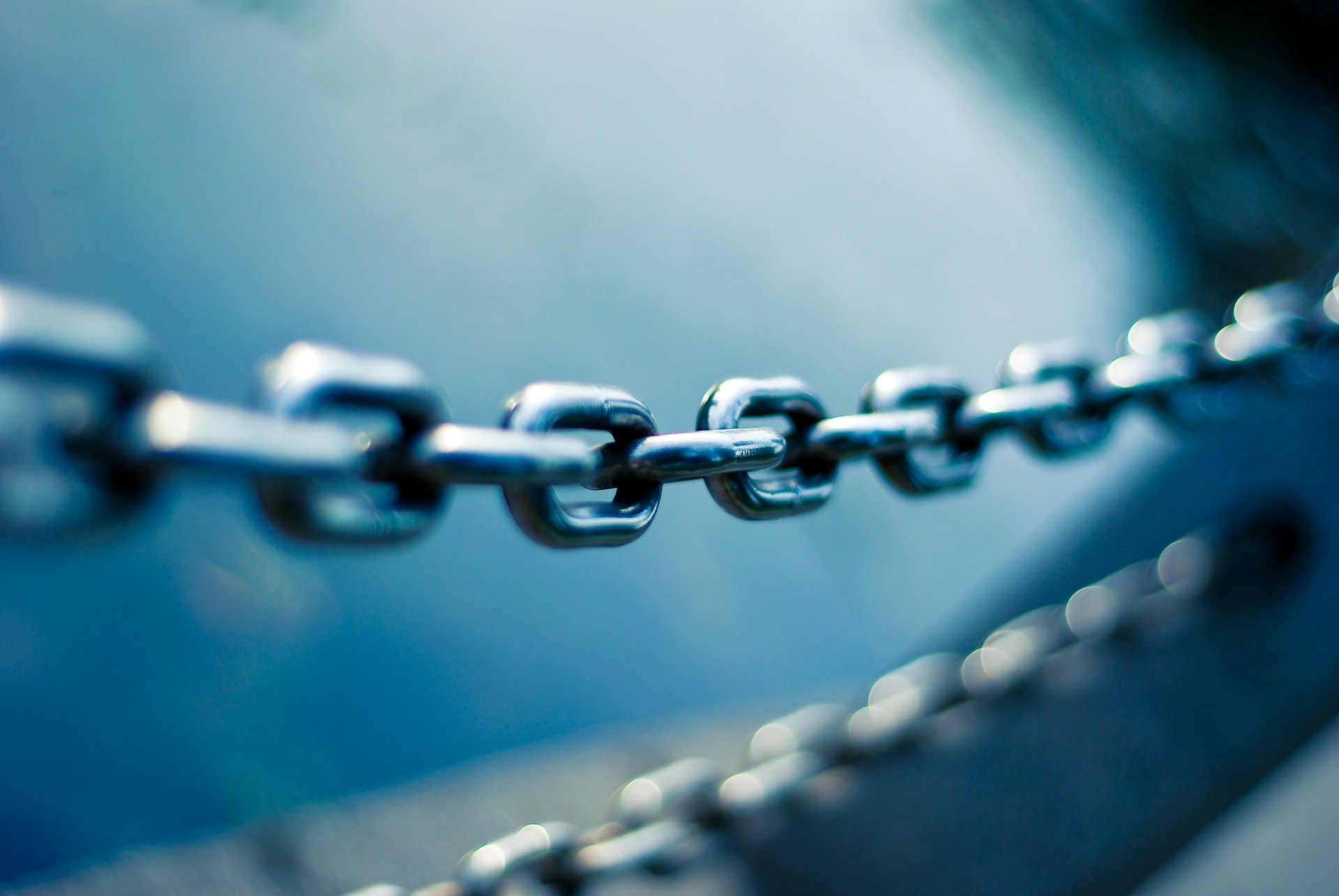 A thick, silver chain stretches over a blue background with a second chain blurred under it, representing Canada's Supply Chain Act and its impact on Vancouver businesses.