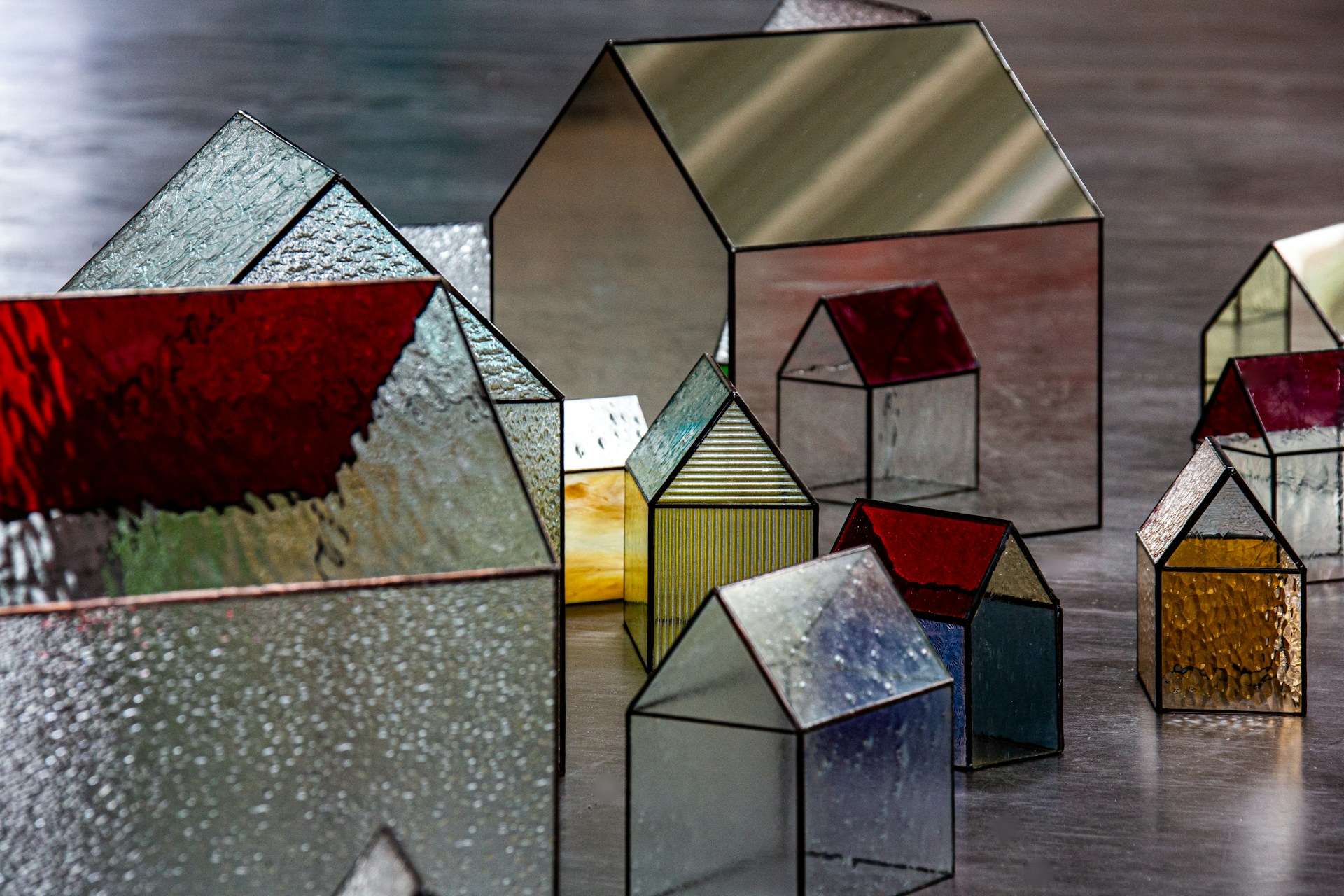 A collection of houses made from stained glass, varying in size, colour, and transparency, representing corporate anonymity.