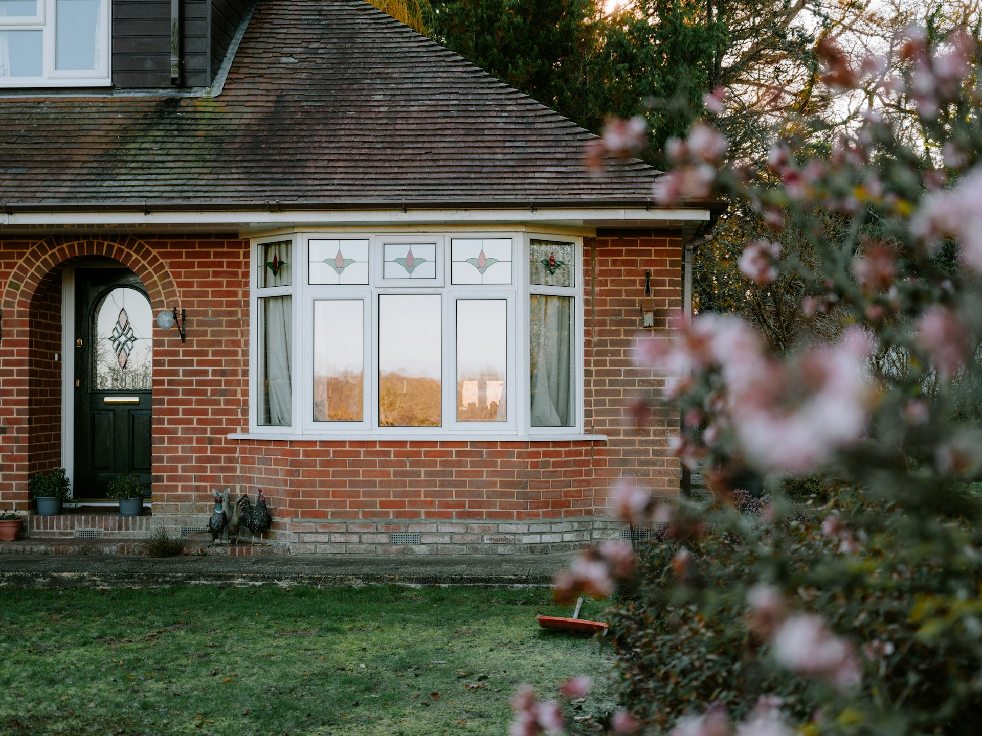 A red brick house with a bay window looking out onto a lawn and blooming bushes, representing real estate purchases and issues that cause delays in real estate closings in British Columbia