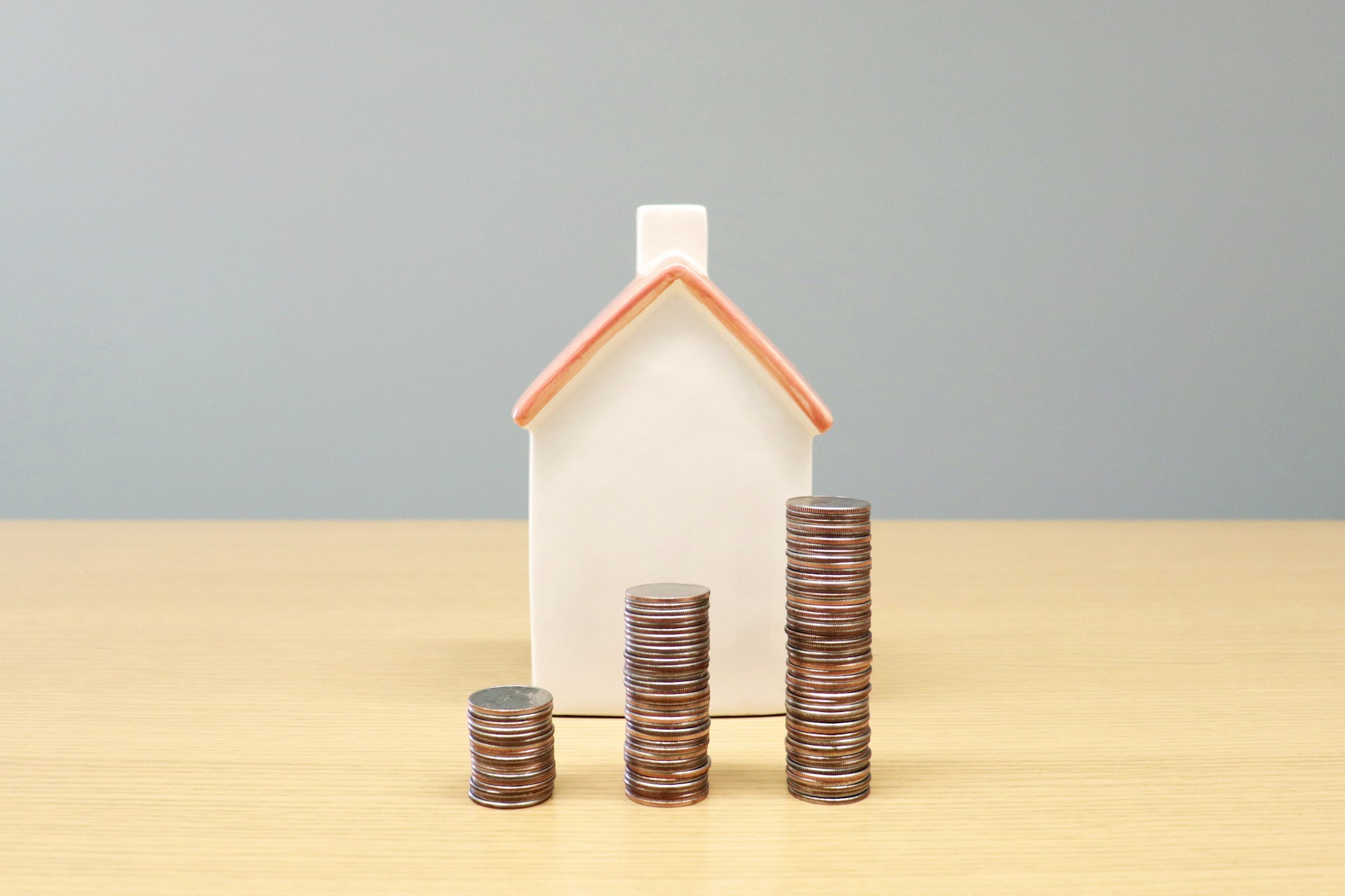 A ceramic house sits on a wood table with small, medium, and large stacks of coins in front of it, representing significant unfair property division.