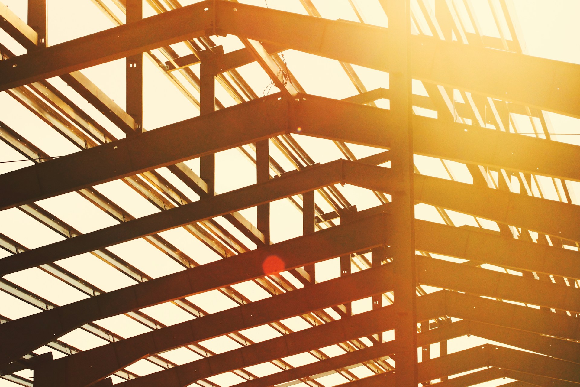 The metal frame of a building under construction's roof with the setting sun glowing between the slats, representing pre-construction assignments in BC.